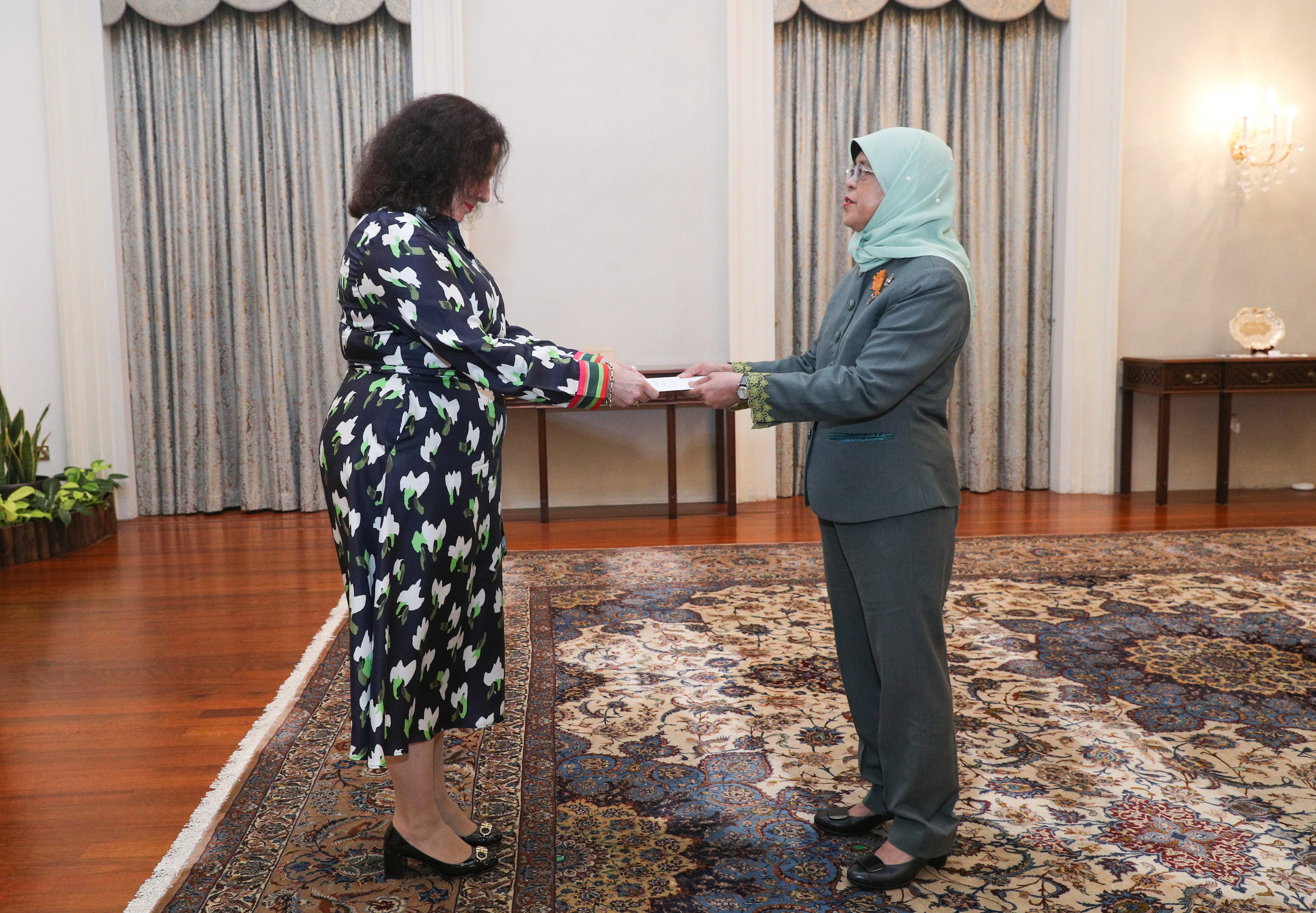 Halimah Yacob receives a document from a woman in a floral dress.